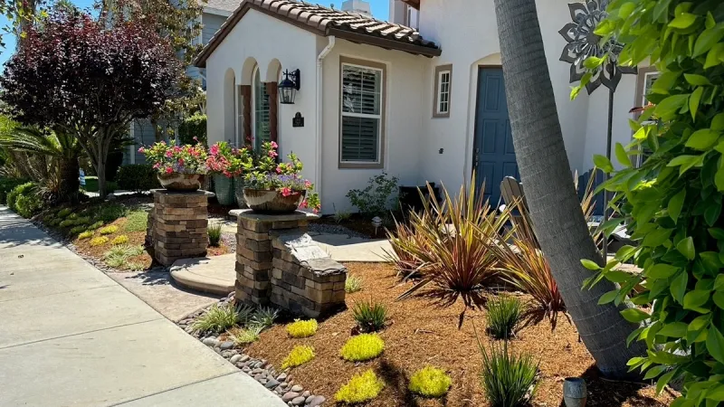 Front yard of a modern house featuring drought-tolerant landscaping with plants, stone pillars, and a pathway.