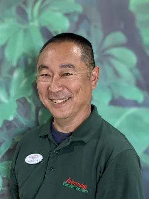Smiling man wearing an Armstrong Garden Centers uniform with greenery in the blurred background