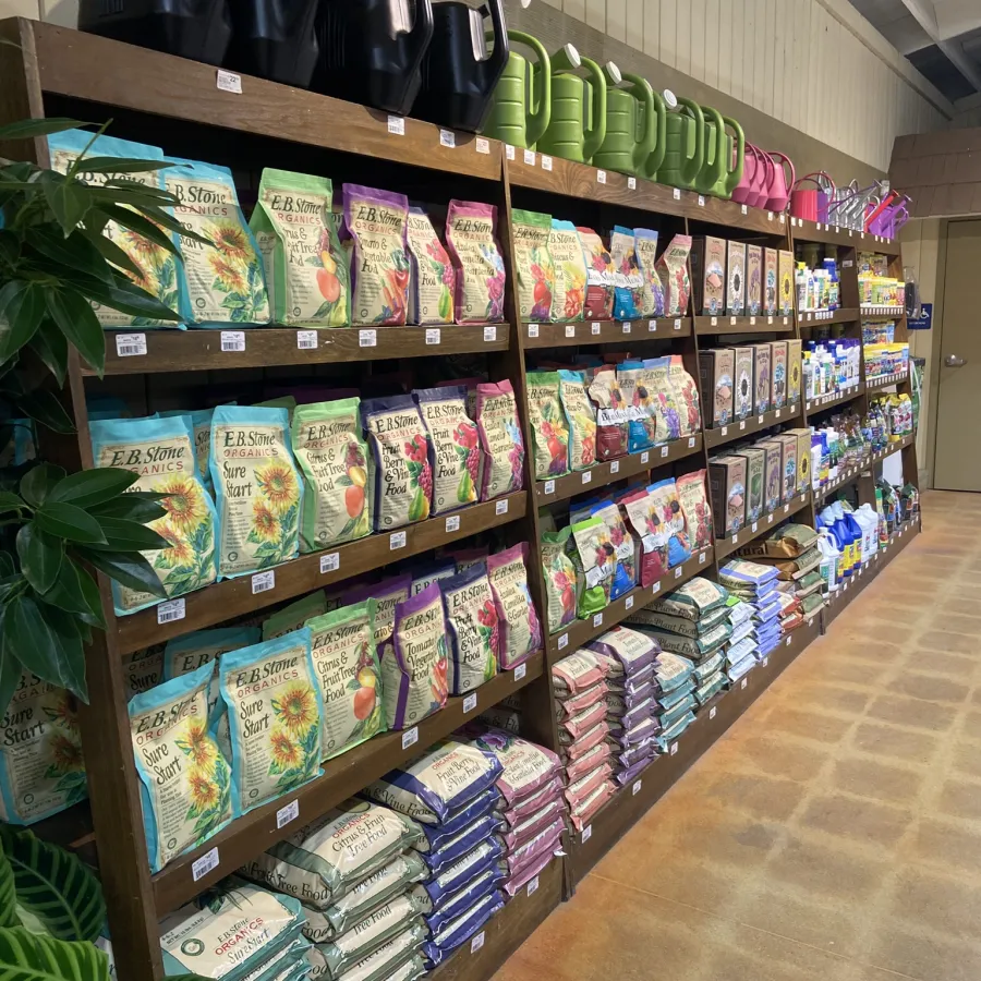 Store shelves stocked with organic gardening supplies, fertilizers, watering cans in various colors, and plant care products.