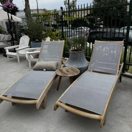 Two modern wooden lounge chairs with gray mesh seats and a small round wooden side table on a concrete patio.