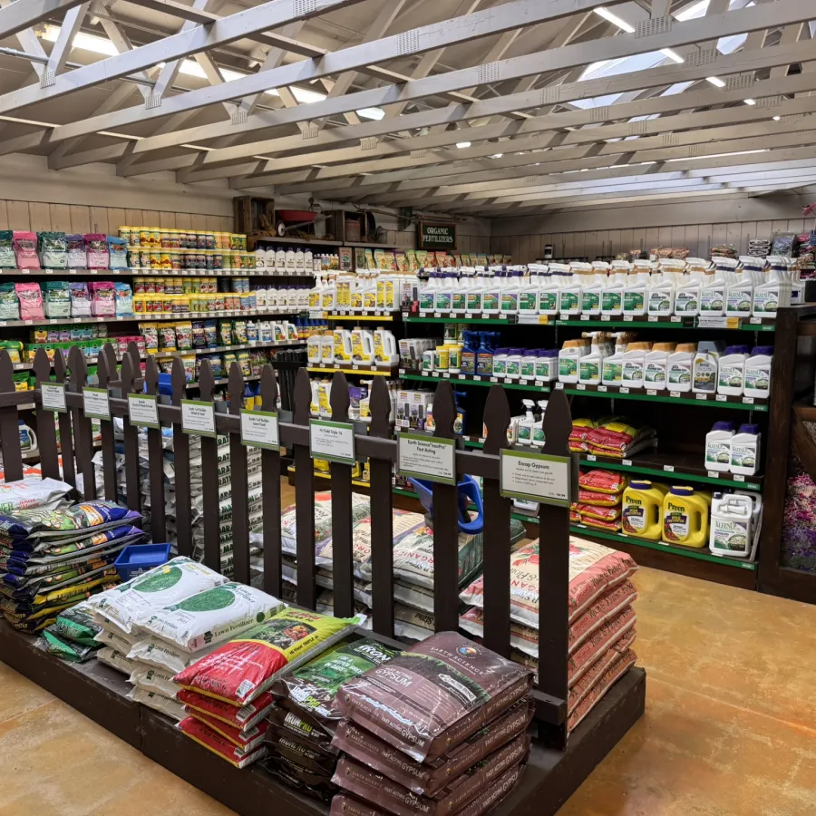 Garden supplies section with shelves of fertilizers, plant foods, and stacked soil bags under a wooden roof.