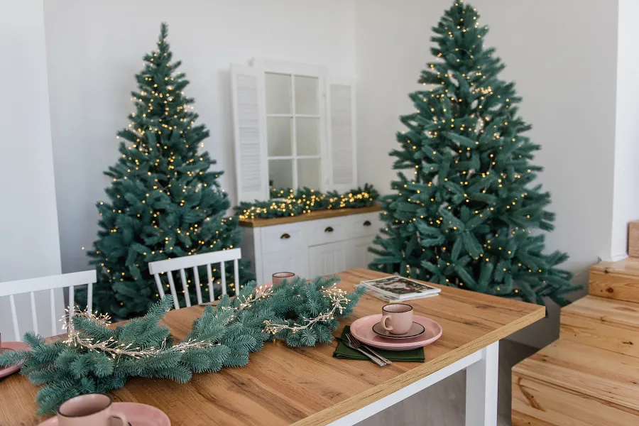 artificial christmas trees with lights in a kitchen with a wood table