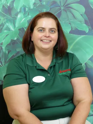 Smiling woman in green Armstrong Garden Centers shirt posing in front of large tropical leaf background.